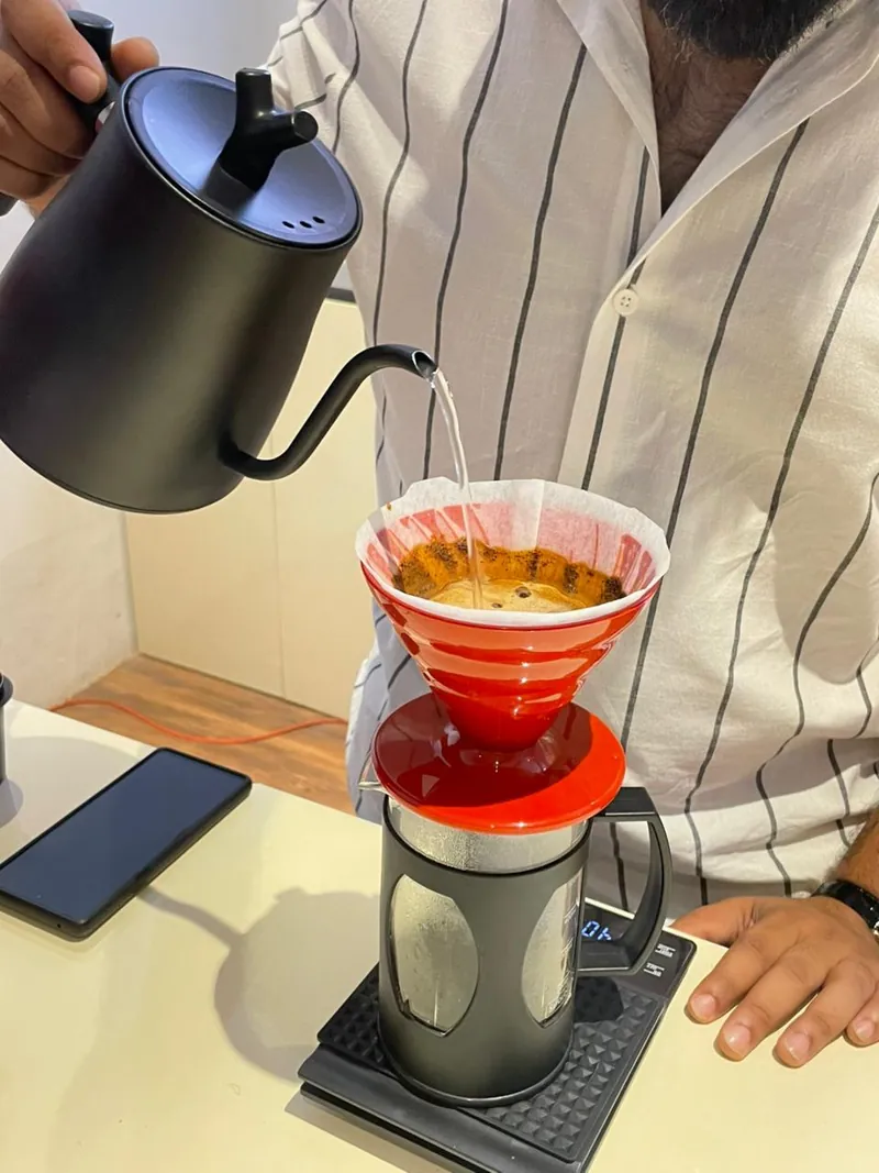 Water poured from a gooseneck kettle over coffee in a red V60 dripper on a scale, during a manual brewing class at The Zariya Academy